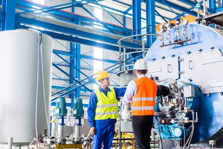 Two engineers wearing safety vests and helmets working in an industrial facility with machinery.