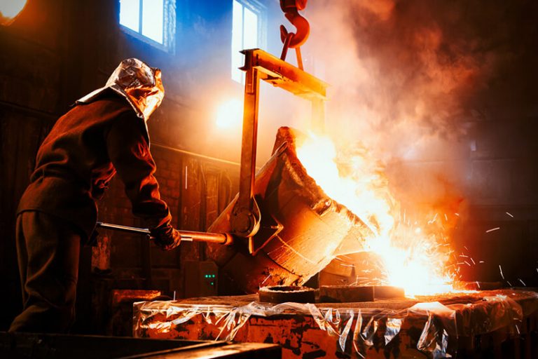 Worker in protective gear pouring molten metal in a high-temperature steel foundry.