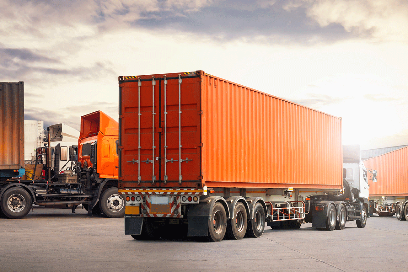 A large orange shipping container mounted on a semi-trailer truck in an industrial yard.