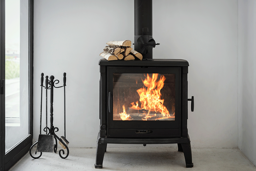 5 A small black wood-burning stove stands in the corner of a room. Its firebox glows warmly with visible flames