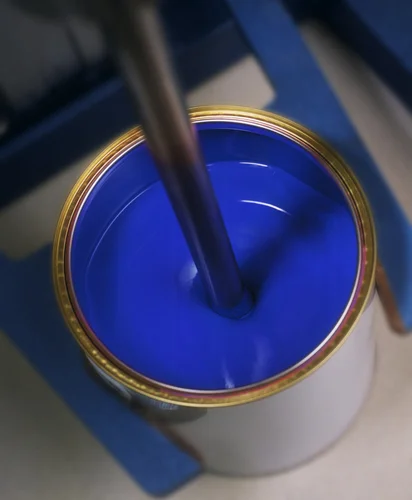 Blue liquid paint in an open can with industrial stirring equipment.