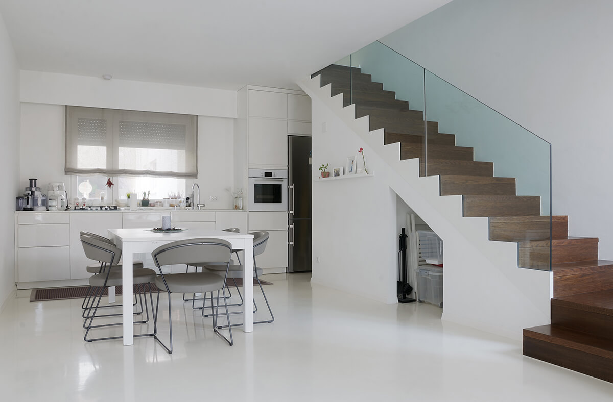 Flooring-solutions2 Minimalist white kitchen interior with wooden staircase, featuring smooth painted walls and modern design elements.
