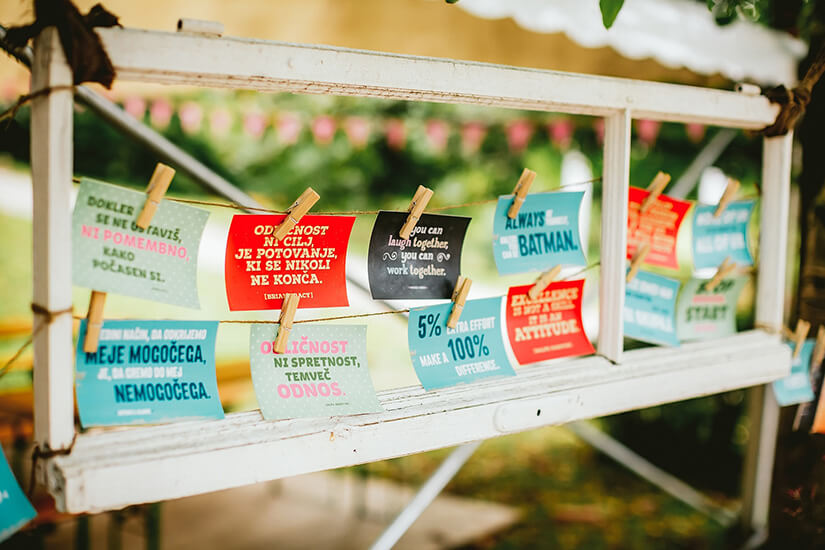 Inclusive-business Colorful motivational quotes in various languages clipped to strings inside a vintage wooden window frame at an outdoor event, promoting inclusive and positive thinking
