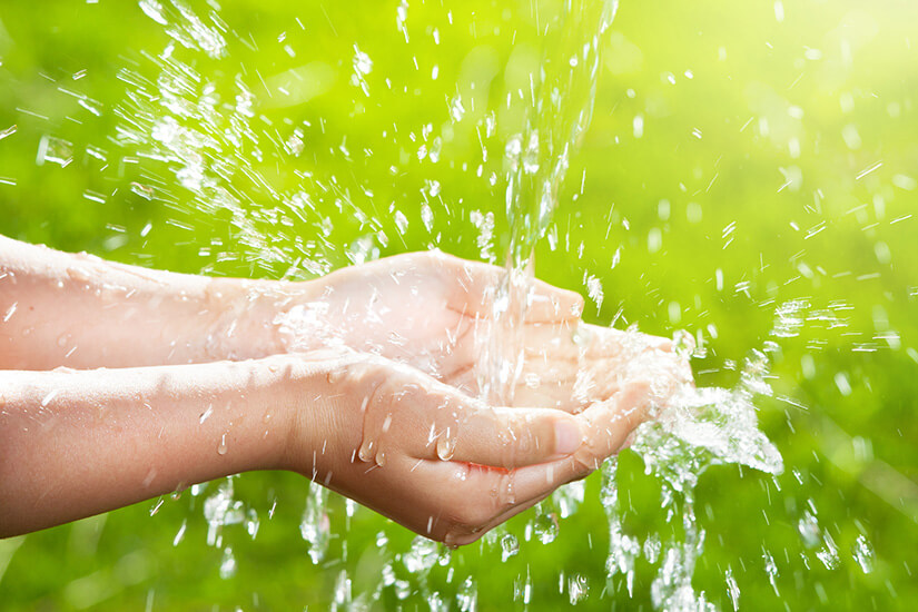 Close-up of hands catching fresh water outdoors, symbolizing clean water access and environmental sustainability.