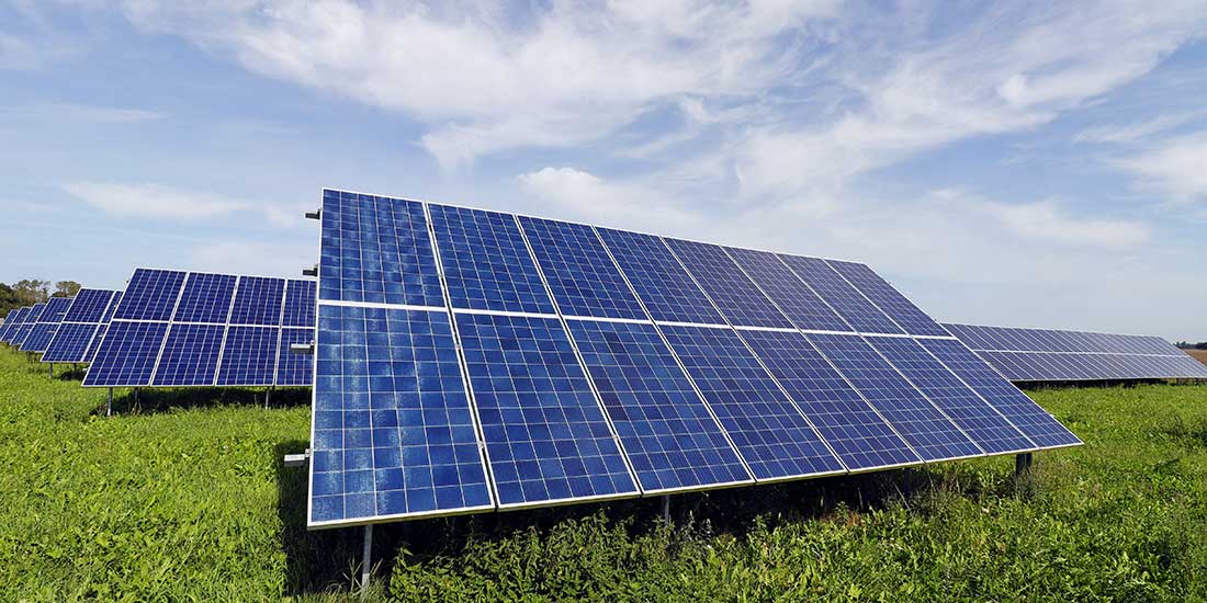Photovoltaic Multiple rows of solar panels are installed on a grassy field, angled to capture sunlight. The sky is partly cloudy above the solar farm.