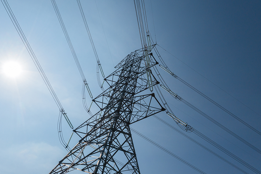 Pylon_shutterstock_2483062071 Close-up silhouette of an electricity pylon with high-voltage power lines against a clear blue sky
