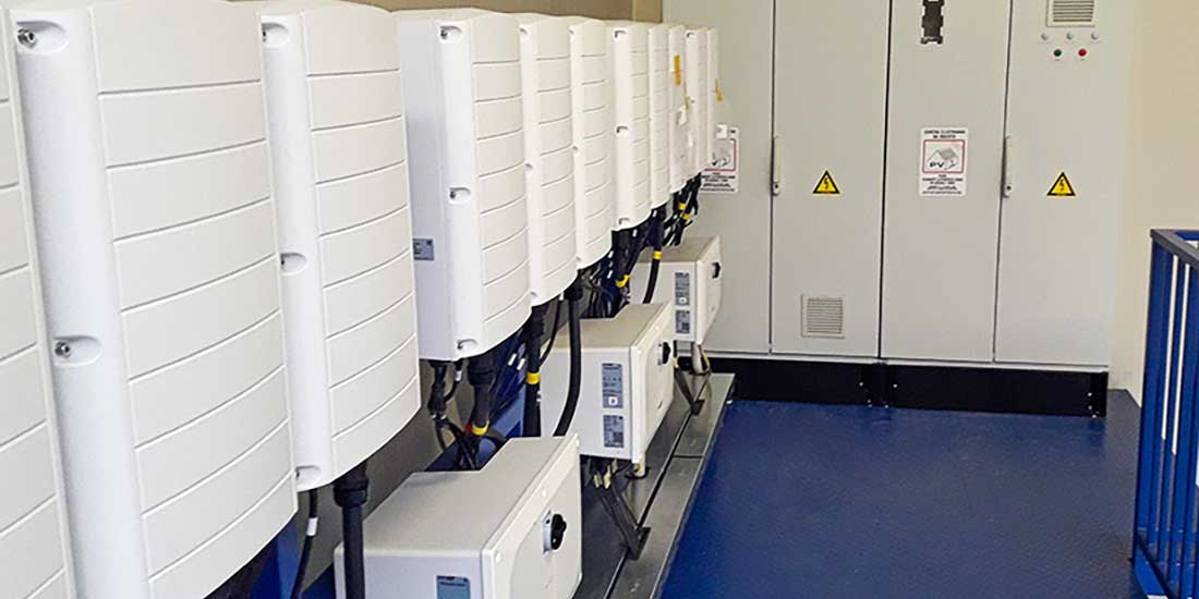 The image shows a row of white electrical cabinets in a solar power plant, used for controlling and converting solar energy.