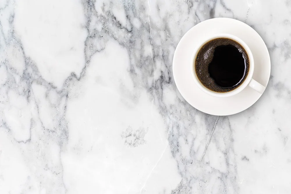 White ceramic coffee cup filled with black coffee on polished marble countertop