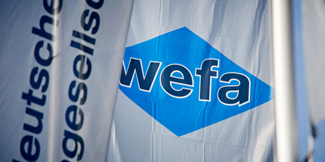 Flag with the word "wefa" in white lowercase letters on a blue diamond-shaped background, next to partially visible text reading "deutsche gesellschaft."