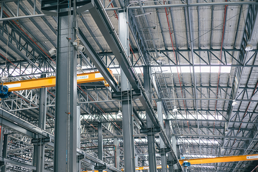 Interior view of an industrial hall under construction with steel beams, metal roof, and overhead cranes.