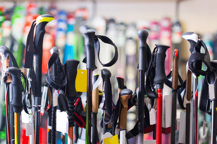 Several ski poles with different grips, colors, and tags standing closely together in a sporting goods store.