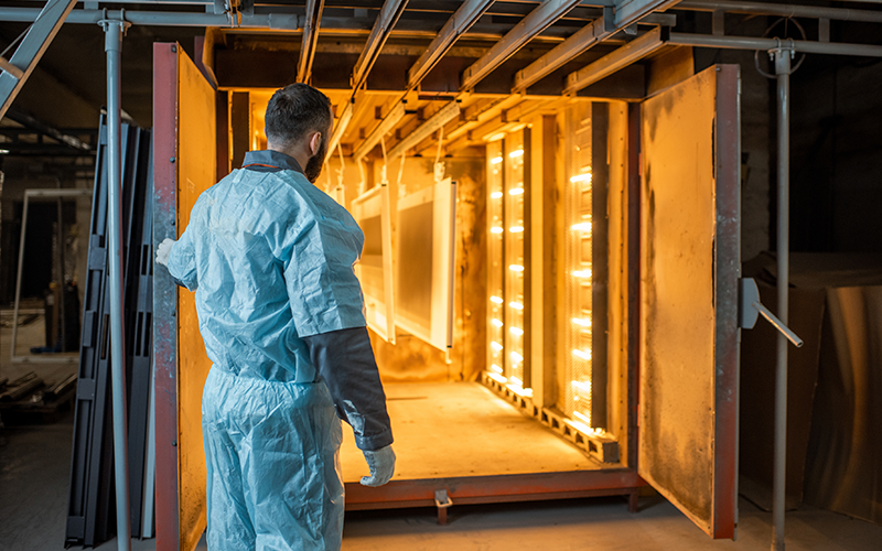 powder-oven man standing in front of an industrial oven waiting for metal parts that are coated with powder coatings to finish baking